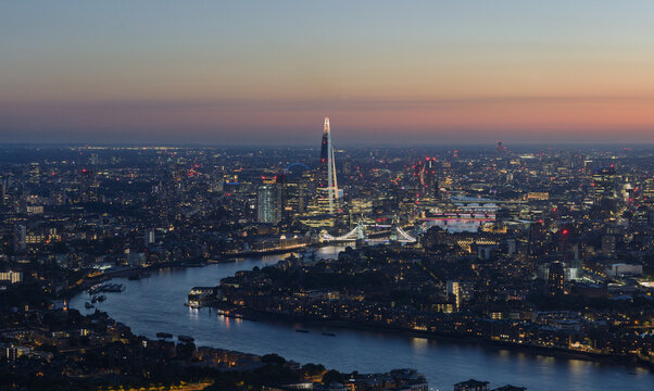 Aerial view of the London skyline at dusk featuring The Shard and Tower Bridge illuminated along the River Thames in London, England, United Kingdom.
