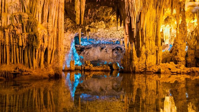 View of Neptune's Grotto featuring intricate stalactites and stalagmites reflected in the calm underground lake, Italy.