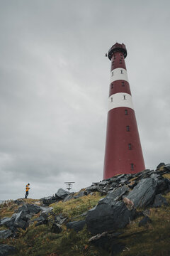 Gamvik, Finnmark, Norway - 26 August 2025: View of Slettnes Lighthouse standing on a rocky coastline under a cloudy sky with a person in a yellow jacket standing nearby.