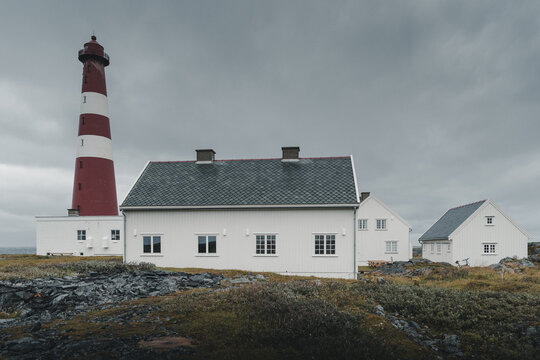 Gamvik, Finnmark, Norway - 26 August 2025: View of Slettnes Lighthouse with its iconic red and white tower standing beside traditional white wooden buildings under a cloudy sky.