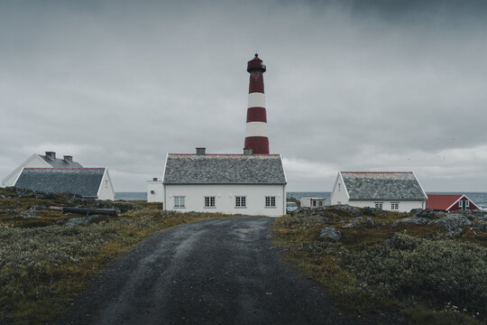 Gamvik, Norway - 26 August 2025: View of Slettnes Lighthouse with its iconic red and white tower, surrounded by traditional white buildings and rocky coastal terrain under a cloudy sky.