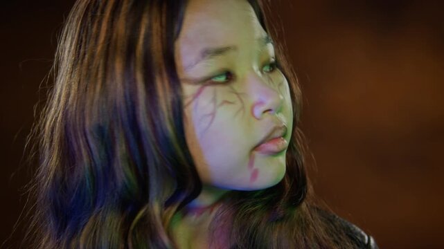 Portrait of Asian teenage girl with zombie Halloween makeup looking at camera and turning head. Footage is ideal for Halloween marketing, horror movie promos, or creative makeup tutorials