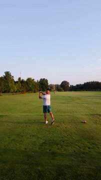 Male golfer in blue shorts and patterned shirt prepares to swing golf club on lush green course under clear sky, showcasing action progression from stance to follow-through