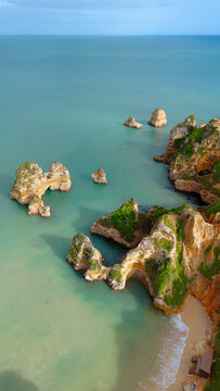 Aerial view of dramatic limestone rock formations and sea stacks at Ponta da Piedade, surrounded by turquoise waters and lush greenery along the coastline. Lagos, Faro District, Portugal.