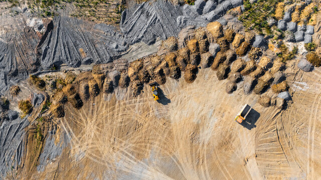 Aerial view of a quarry site with heavy machinery including a bulldozer and a dump truck operating among piles of earth and gravel with tire tracks visible in Beocin, Vojvodina, Serbia.