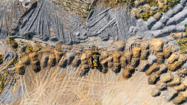 Aerial view of a yellow bulldozer working at a quarry with piles of gravel and earth, tire tracks on the ground, and excavated terrain in Beocin, Vojvodina, Serbia.