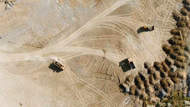 Aerial view of a quarry site with heavy machinery and dump trucks moving across dusty ground marked by tire tracks in Beocin, Vojvodina, Serbia.