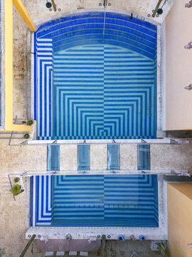Aerial view of a swimming pool with a geometric blue and white striped tile pattern, surrounded by stone decking in Valladolid, Yucatan, Mexico.