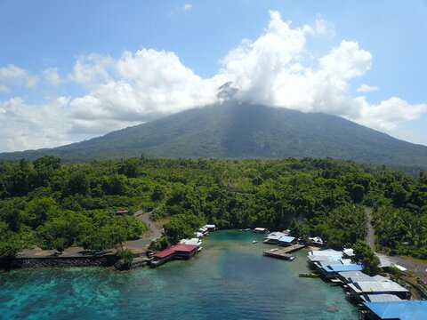 Aerial view of the coastal village of Ternate at the base of Gamalama volcano, featuring stilt houses over turquoise waters and lush tropical vegetation in Ternate, North Maluku, Indonesia.