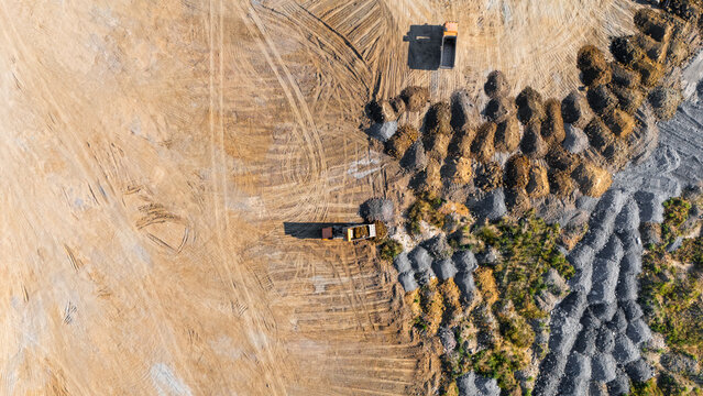 Aerial view of a quarry site with dump trucks moving soil and gravel, featuring piles of excavated material and tire tracks in Beocin, Vojvodina, Serbia.