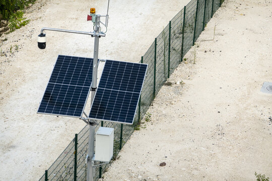 View of a solar-powered security camera pole with surveillance equipment and warning light installed along a wire fence in the rural landscape of Calakmul, Campeche, Mexico.