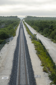 View of the Tren Maya railway tracks stretching through the dense jungle landscape with gravel ballast and protective fencing in Calakmul, Campeche, Mexico.