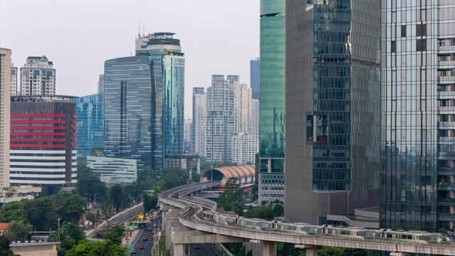 Aerial view of the modern skyline with glass skyscrapers, a monorail track with a train, and urban roads in Jakarta, Indonesia.