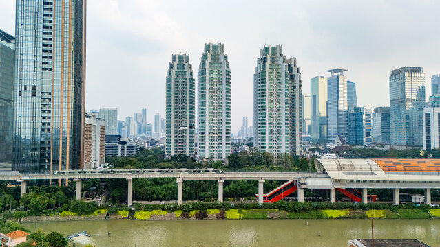 Aerial view of the Jakarta skyline featuring modern skyscrapers, the MRT train on an elevated track, and the river flowing through the urban landscape in Jakarta, Indonesia.