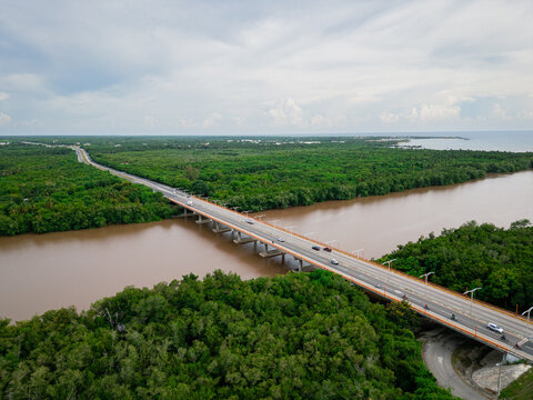 Aerial view of the Rio Soco bridge spanning the river, surrounded by lush mangroves and tropical vegetation under a cloudy sky in San Pedro de Macoris, San Pedro de Macoris, Dominican Republic.