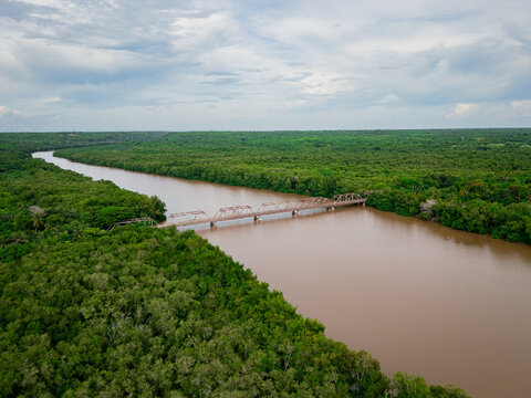 Aerial view of the historic iron bridge spanning winding Rio Soco surrounded by dense tropical forest under a cloudy sky in San Pedro de Macoris, San Pedro de Macoris, Dominican Republic.