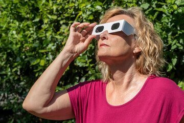 Obraz premium Blonde woman in red observes the sun with classic solar eclipse protective glasses
