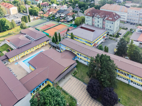 Aerial view of Zakladna Skola Dr. V. Clementisa featuring colorful school buildings, a swimming pool, tennis courts, and surrounding greenery in Tisovec, Gemer, Banskobystrick, Slovakia.