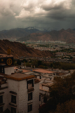 View of the Potala Palace with its traditional white architecture set against a dramatic cloudy sky and the surrounding mountain landscape in Lhasa, Tibet, China.