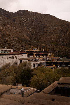 View of the traditional Tibetan architecture of the Potala Palace complex nestled against a rugged mountain slope under an overcast sky in Lhasa, Tibet, China.