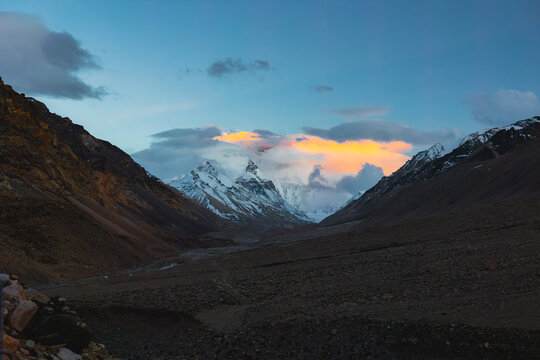 View of Mount Everest from the view point with snow-capped peaks, golden clouds at sunset, and rocky valley terrain in Tibet, China.