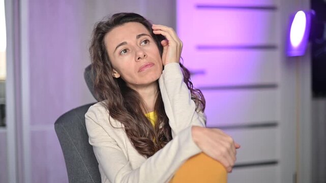 Frustrated young woman feeling bored and lonely while sitting alone in a modern purple lit room and thinking about her problems