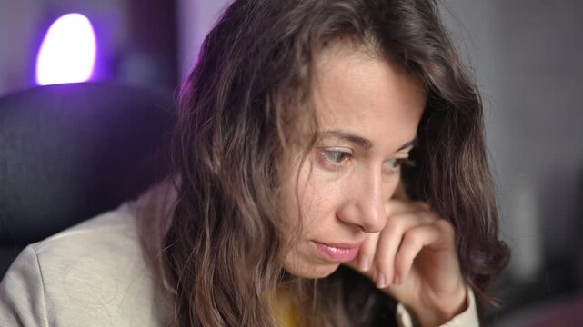 Stressed and pensive woman thinking about problems while working on a computer at night with purple led lights in background