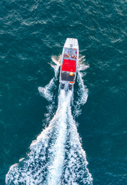 Aerial view of a motorboat with a red canopy cruising through the deep blue sea, leaving a white wake behind it in Herzliya, Tel Aviv District, Israel.