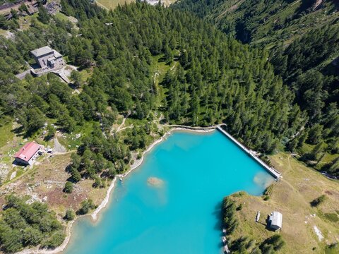 Aerial view of Wasserkraftwerk Palu and its turquoise reservoir surrounded by dense pine forests and steep mountain slopes in Poschiavo, Grisons, Switzerland.