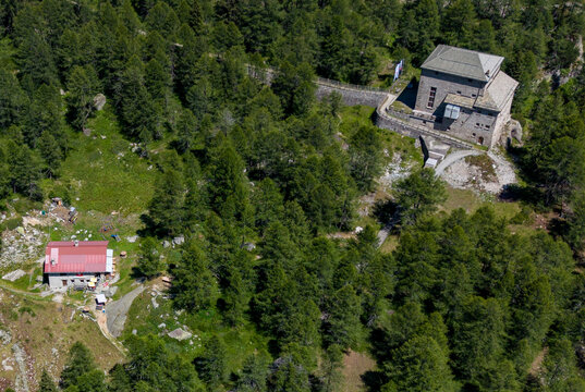 Aerial view of the Wasserkraftwerk Palu hydroelectric power plant nestled within a dense coniferous forest in the mountainous landscape of Poschiavo, Grisons, Switzerland.