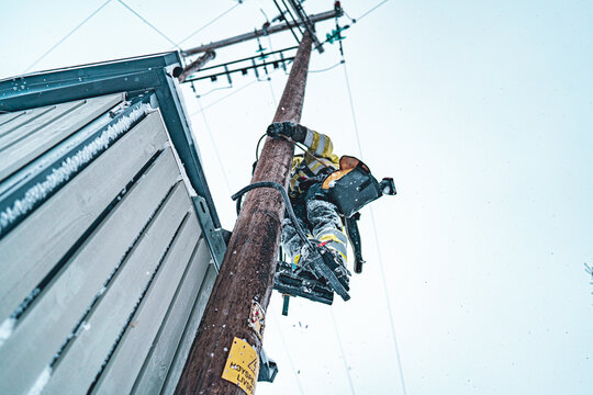 Tromso, Troms, Norway - 05 February 2020: View of a utility worker climbing a wooden utility pole to perform maintenance on power lines during a snowy winter day.