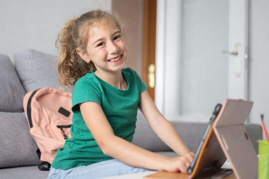 Smiling schoolgirl using tablet for online learning at home