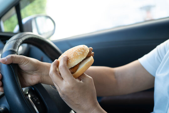 Asian woman driver hold and eat hamburger in car, dangerous and risk an accident.