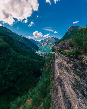Aerial view of Geirangerfjord surrounded by steep mountains, lush green forests, and deep blue water in Stranda Municipality, More og Romsdal, Norway.