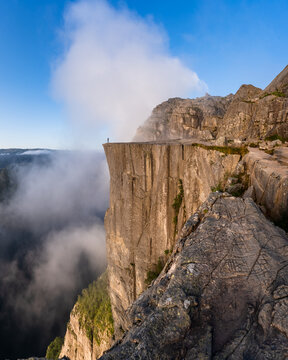 View of Pulpit Rock with a lone hiker standing on the edge of the massive cliff overlooking the clouds and deep fjord in Strand, Rogaland, Norway.