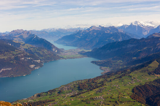 Aerial view of Niesen Hiking View Point overlooking Lake Thun, surrounded by green slopes, alpine villages, and snow-capped peaks in Reichenbach im Kandertal, Canton of Bern, Switzerland.