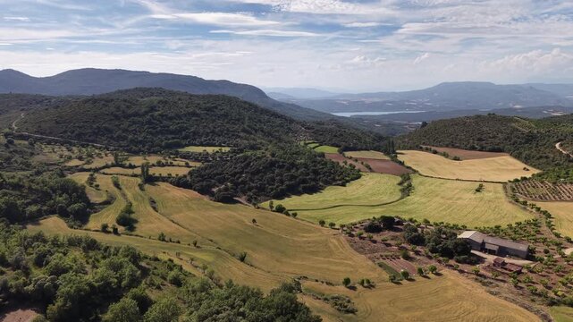Aerial footage of scenic valley with farmland in Spanish Pyrenees. Summer landscape with mountains with lake in the background. 