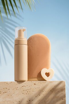Self tanning mousse bottle and applicator mitt on stone pedestal. Sunless tanner product display with heart stencil against blue sky. Summer skincare concept