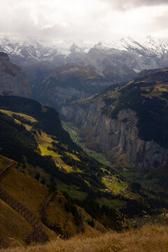 View of Kleine Scheidegg overlooking the deep Lauterbrunnen valley with snow-capped peaks, steep cliffs, and lush green meadows in Lauterbrunnen, Canton of Bern, Switzerland.