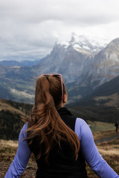 View of a woman with long brown hair in a ponytail looking out at the majestic snow-capped peaks of Kleine Scheidegg in the Swiss Alps, Lauterbrunnen, Canton of Bern, Switzerland.
