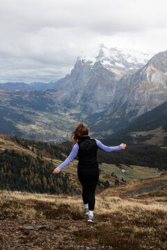 View of a woman standing with arms outstretched overlooking the Kleine Scheidegg mountain pass with snow-capped peaks and the valley of Lauterbrunnen, Canton of Bern, Switzerland.
