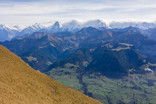 View of the Niesen mountain range with snow-capped peaks, rolling green alpine meadows, and forested slopes in the valley, Reichenbach im Kandertal, Canton of Bern, Switzerland.