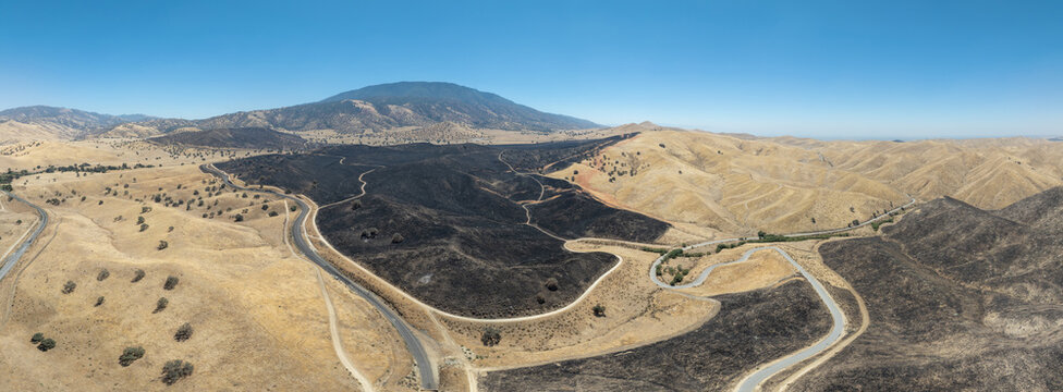 Aerial view of the Caliente Fish Fire burn area showing scorched black earth contrasting with dry golden hills and a winding road in Caliente, CA, United States.