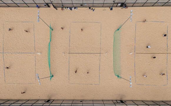 Aerial top-down view of multiple beach volleyball courts with players on sand, outdoor urban sports facility and recreation concept.