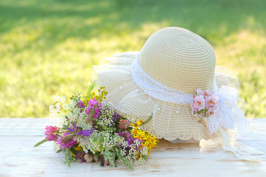 Beautiful wildflowers bouquet and summer braided hat close up on table in garden, sunny natural background. relax, harmony, meditation, romantic atmosphere. spring, summer blossom season.