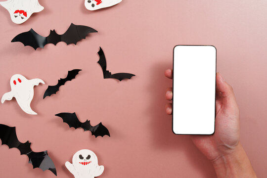 Cropped hand holding smartphone with blank screen near Halloween paper bats and ghosts