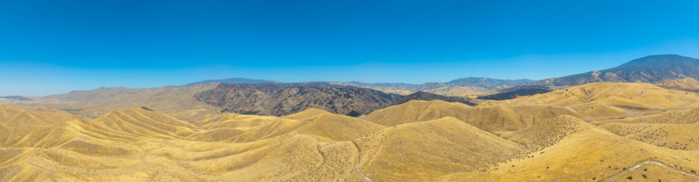 Aerial view of the Caliente Fish Fire burn area showing scorched earth and dry golden rolling hills under a clear blue sky in Caliente, CA, United States.