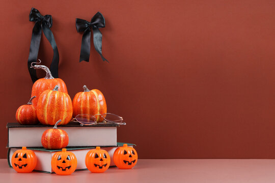 Halloween still life with decorative pumpkins and books on brown background with copy space