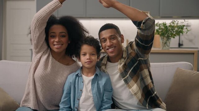 Happy African American family couple son showing roof gesture in apartment portrait loving ethnic woman man join hands over head adopted little child kid looking camera cozy adoption buying new home