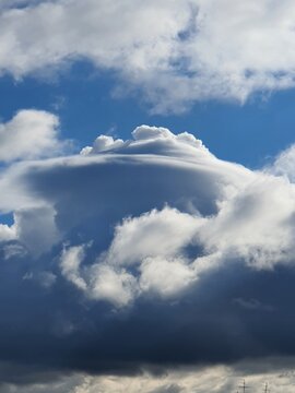 Rare pileus cloud forming a smooth cap over a developing cumulonimbus thunderstorm cloud against a blue sky. Unusual atmospheric phenomenon captured in natural daylight.
